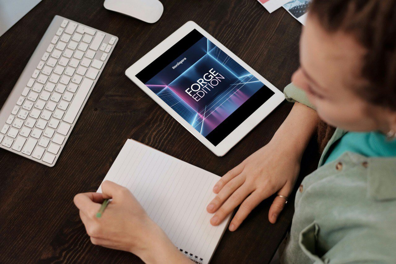 Person using a 'forge Edition' guide on a tablet with a keyboard and notebook on a wooden desk